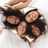 four women of mix race with camera capturing a ground up image that shows all of their heads coming together in a circular way