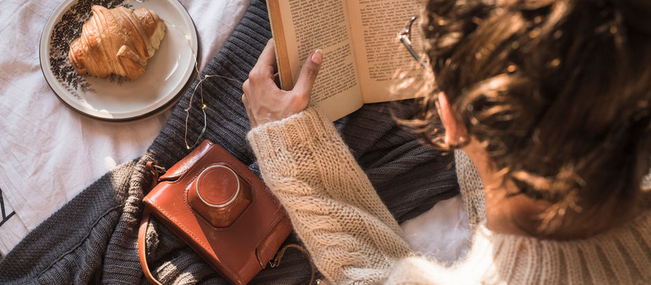 Osoba w swetrze czyta książkę przy talerzyku z rogalikiem – idealny poranek z książką na jesień