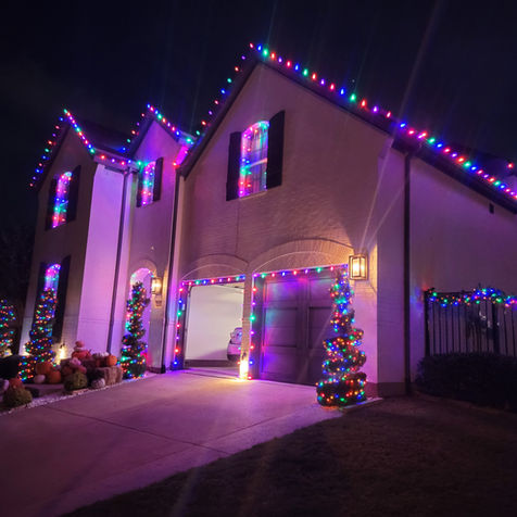 Christmas lights along the gutterline of the white house with multicolor lights wrapped around front trees.