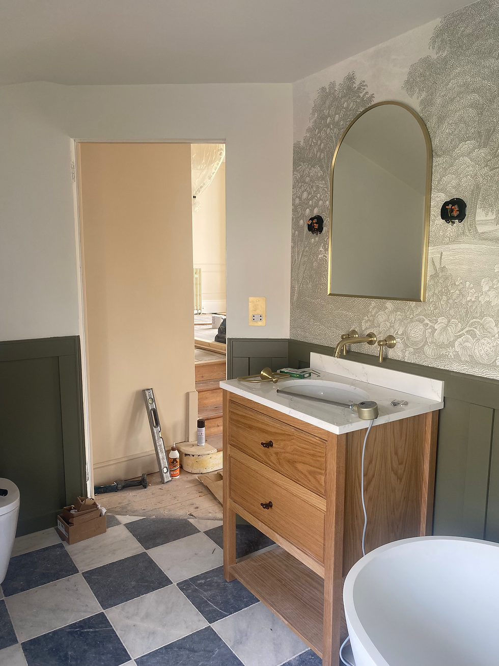 Master Ensuite Bathroom in a Georgian Listed Home. Oak vanity unit with dark green half height panelling, green foliage Muriel and brass arched mirror.
