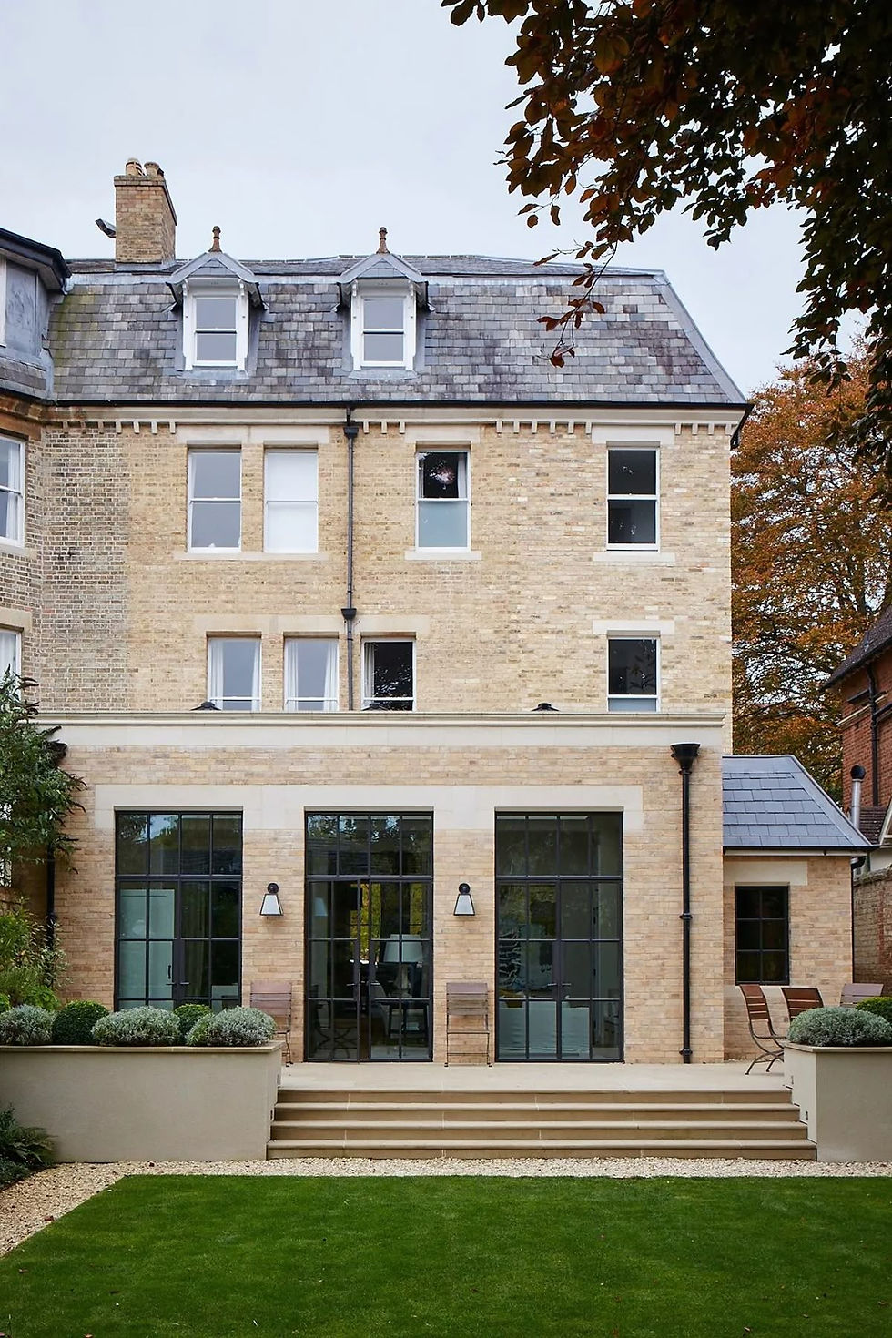 A period home with a modern extension at the rear with three windows and a green landscaped garden