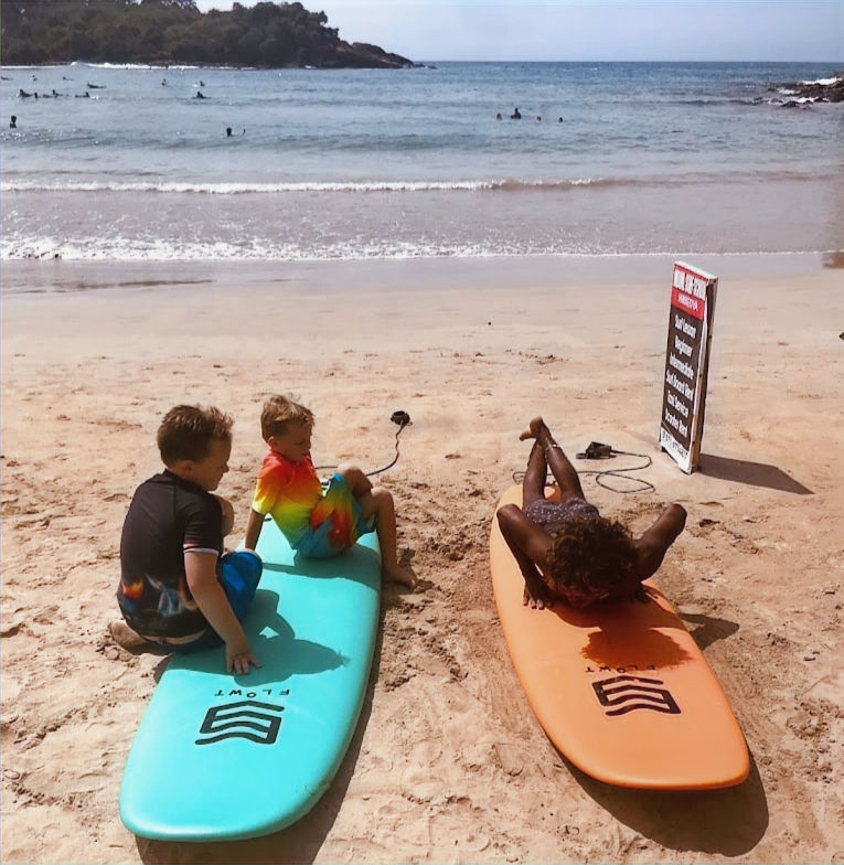 Sachee demonstrating land-based surf techniques with kids at Hiriketiya Beach, ensuring they feel prepared and excited to tackle the waves together.