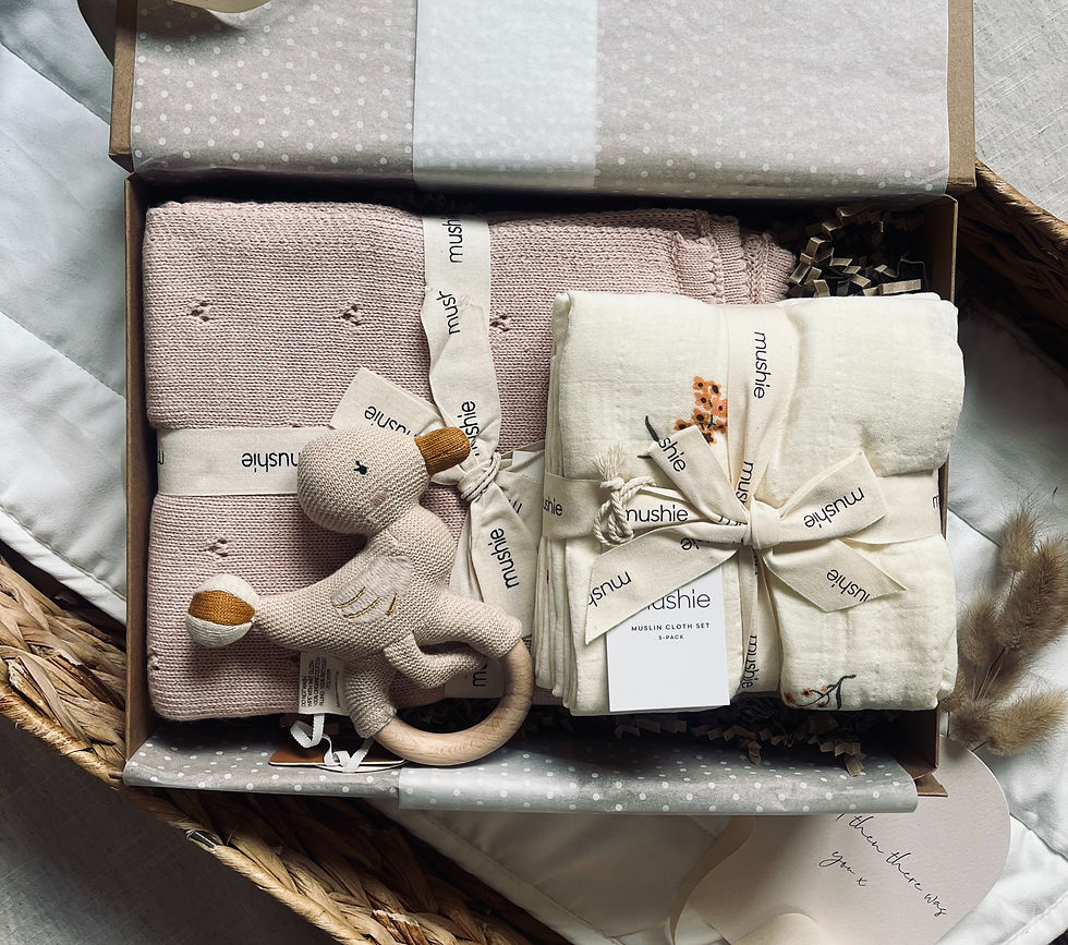 baby gift box containing a blush pink Mushie pointelle blanket, tied 3-pack floral muslin cloths, and a knitted wooden rattle