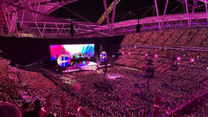 Coldplay Music of the Spheres Tour 2025 at Wembley Stadium in London, with the stage lit up in vibrant colors and thousands of fans wearing glowing LED wristbands.
