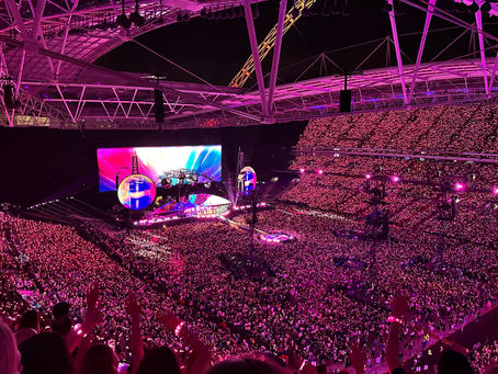 Coldplay Music of the Spheres Tour 2025 at Wembley Stadium in London, with the stage lit up in vibrant colors and thousands of fans wearing glowing LED wristbands.