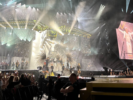 Robbie Williams performing on stage in Kaunas at Darius and GirÄ—nas Stadium, with stage lights and fans in the foreground