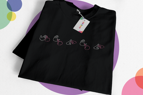 A black t-shirt with a graphic on the upper chest. The graphic is of BSL finger spelling, the colours are pink and white. There is no translation on the t-shirt, but the finger spelling says “IYKYK”. There is a tag on the shirt that shows Anvil Inc’s logo.