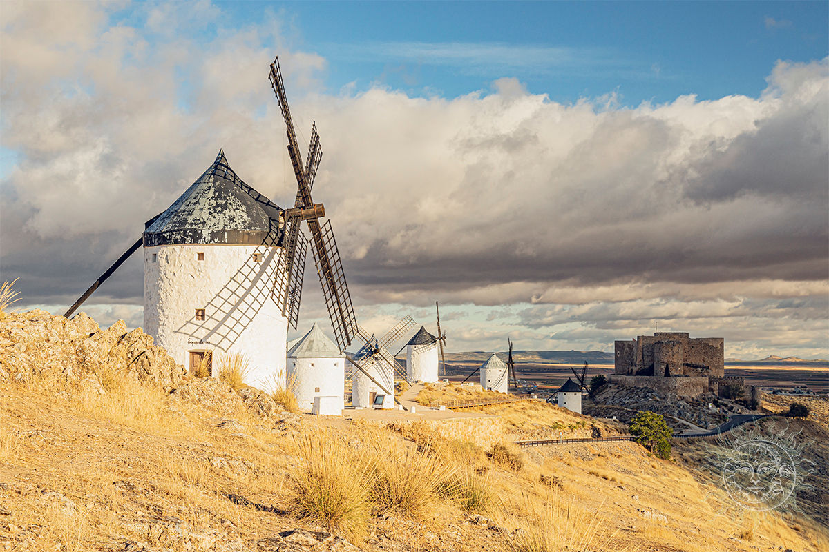 Historic windmills and castle on a hill under a dramatic cloudy sky