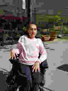 Lidija Ljubic in einem sonnigen Vorhof im Rollstuhl sitzend mit rosa Pullover