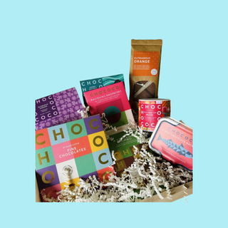 Branded chocolate gift hamper featuring assorted premium chocolate bars, tins and packaged treats arranged in a presentation box with shredded paper filling.