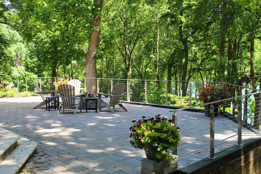 Multi-level paver patio with outdoor seating and wooded backdrop installed by Yard Shark Lawn Care