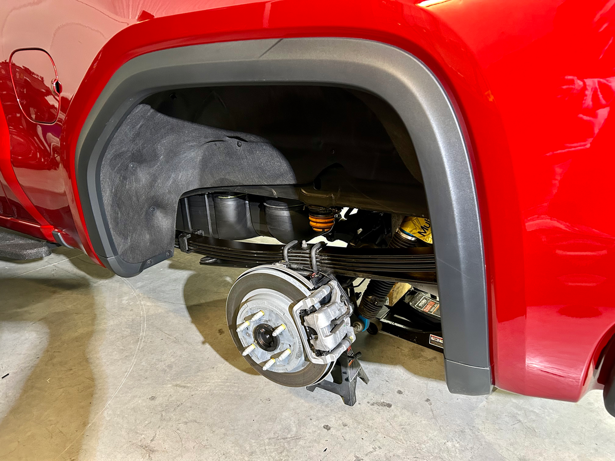 Red truck's rear wheel well displaying brake rotor, caliper, and suspension.