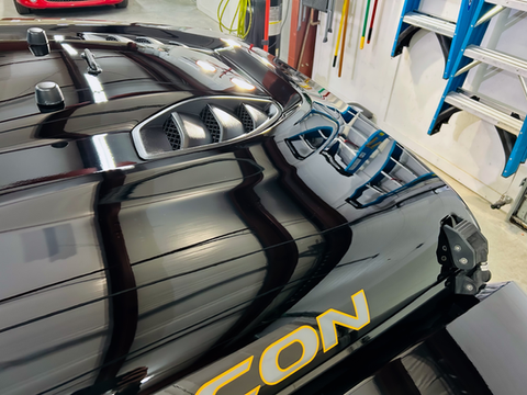 Shiny black vehicle hood with vents, orange 'CON' text, reflecting garage.