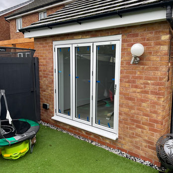 Backyard with artificial turf showing a closed white patio door with protective blue tape.