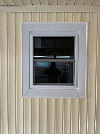 White framed square window reflecting the surroundings against a beige wall.
