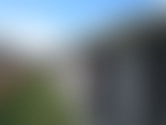 Seamless Gutters Brick house with white gutters, wooden fence, and grassy side yard under a bright blue sky with clouds. Patio chairs are visible.