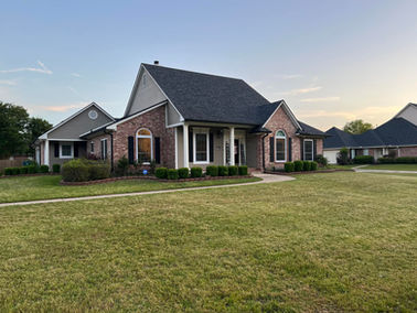 Residential home with brick and black roof, green lawn, in the distance, Blazier Unlimited.