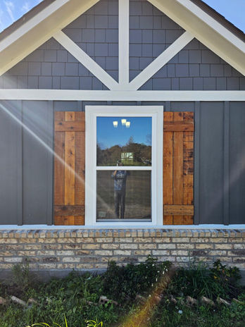 Exterior home view with wooden shutters and window; blue siding, house. Blazier Unlimited.
