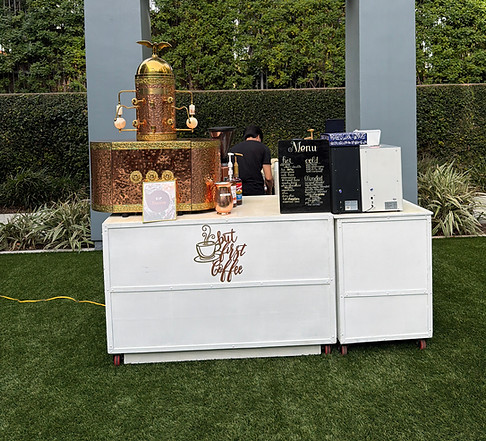 A mobile coffee set up with copper structure, menu, different syrups and it is on grass landscaping.