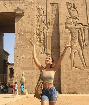 Jeune fille levant les mains devant le temple d’Edfou, Égypte, imitant les pharaons égyptiens.