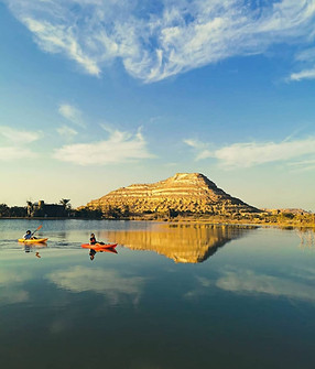 Profitez d’une aventure dans l'oasis de Siwa en kayak sur des eaux calmes avec une vue imprenable sur une colline majestueuse, reflétée parfaitement sous un ciel bleu.