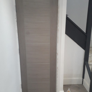 Grey laminated door fitted to under-stairs cupboard. Stair stringer and post painted black.