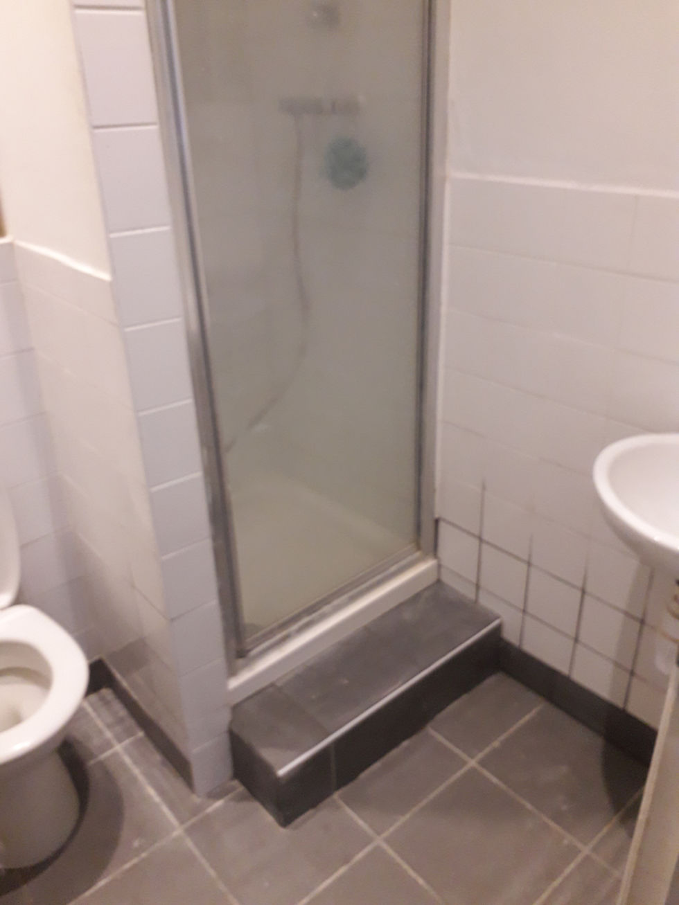 Small bathroom with tiled floor, white tiled walls, a shower with glass door, a toilet, and a sink. Gray and white color scheme.