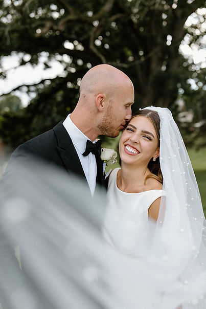 Bride and Groom pose behind a pearl veil on their wedding day in Wisconsin
