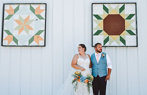 Bride and Groom posing in front of hand painted barn quilts at Wisconsin Barn Venue