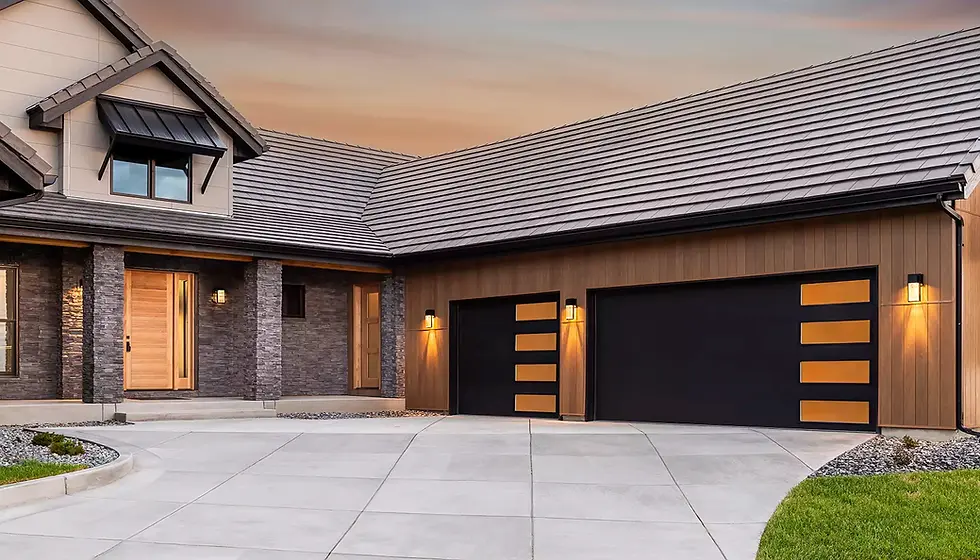 Modern home exterior featuring two black contemporary garage doors with horizontal glass panels, wood siding, stone accents, and a wide concrete driveway at sunset.