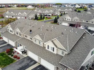 Aerial view of a multifamily townhouse community with a roofing contractor performing a roof inspection on a large residential building.