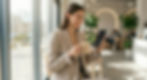 A candid style photograph of a young professional woman sitting in a stylish, sunlit cafe.