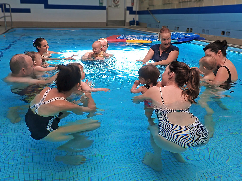 Group of six parents in a circle hold their babies during a swimming lesson as swimming teacher Anat Juran leads the class