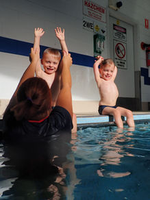 Swimming instructor teaching two kids how to make rocket hands on the pool edge