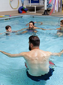 Group of parents and toddlers in a circle with swimming teachers in a pool