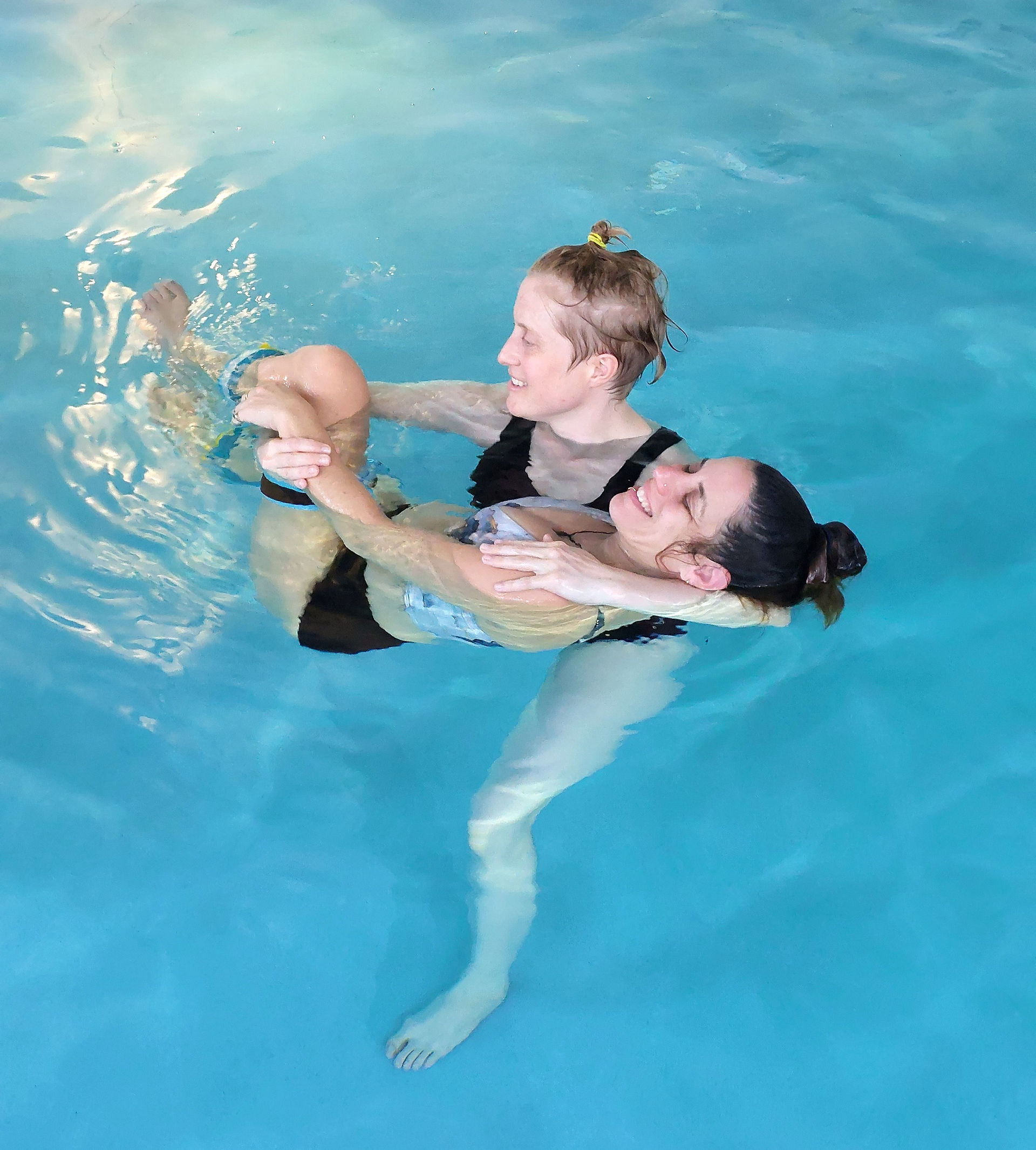 a blond woman is holding another woman with dark hair who is smiling in a pool