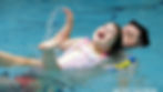Child in a swimsuit joyfully splashes in a pool, supported by an adult. Blurred background, blue water, text reads: "Aquatic Bodywork."
