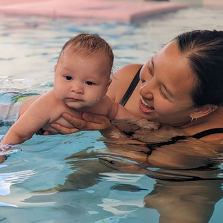 Woman joyfully holds baby swimming in a pool. Clear water surroundings, baby in swim diaper. Text "© Aquanat" visible.