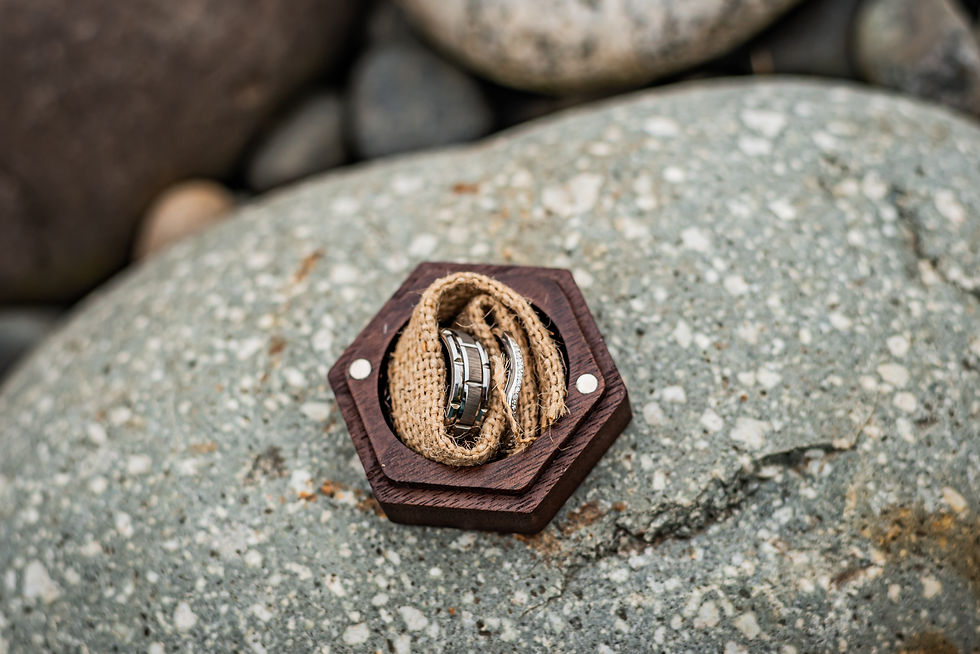 Hexagonal wood box on speckled rock holds two silver rings in burlap. Natural setting with muted colors, evoking a serene mood.