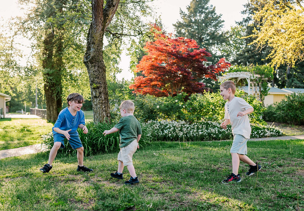 Three boys play on grass under trees, with vibrant red leaves in the background, in a sunny, green park setting, smiling and cheerful.