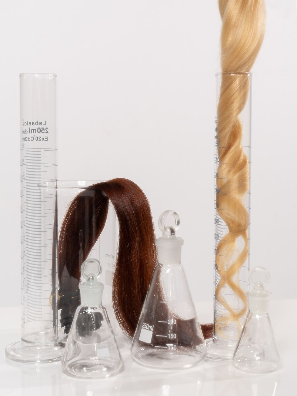 Glass lab beakers with long strands of brown and blonde hair inside are set against a plain white background.