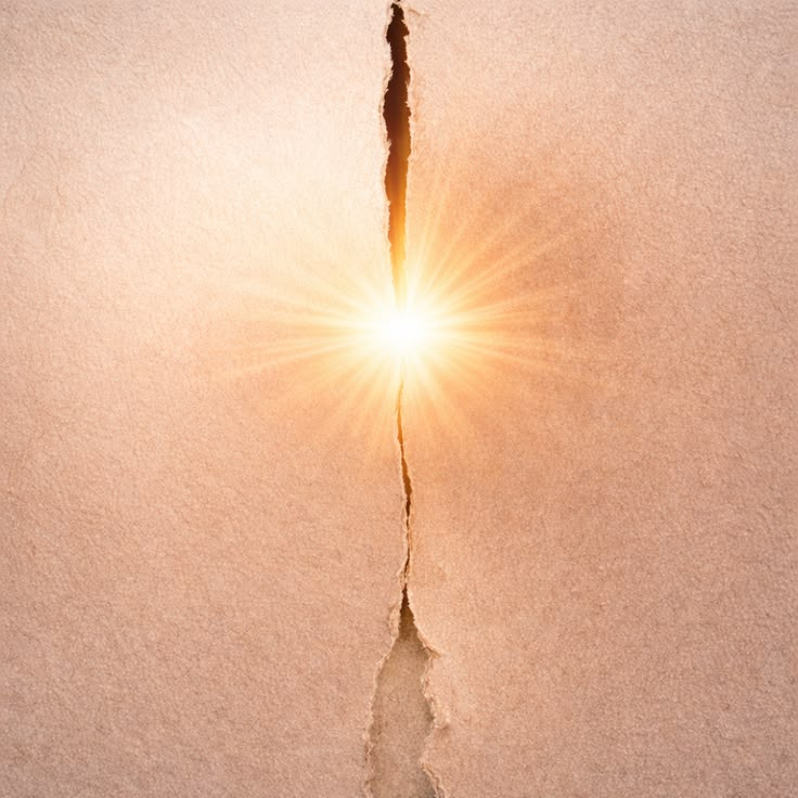 A bright light shines through a torn brown paper, creating a glowing effect. The tear is vertical, with textured paper edges.