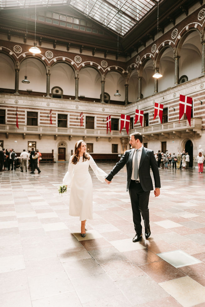 Joyous bride and groom exiting Copenhagen City Hall, hand in hand, as they embark on their new journey together amidst confetti and cheers