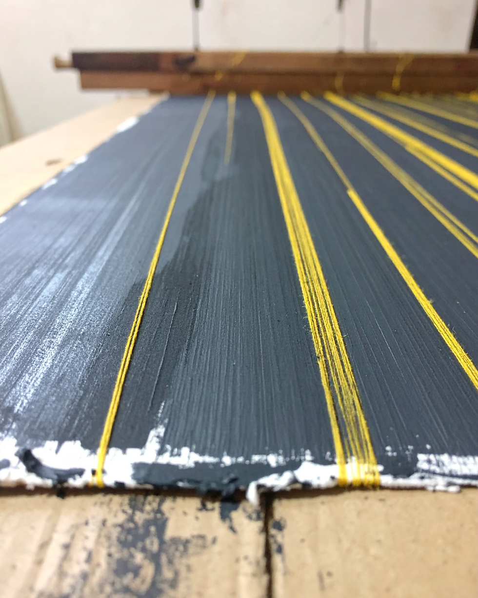 Mit schwarze eingestriche Pappe mit gelben Fäden umspannt.