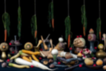Dark still life of hanging carrots, radishes, beets, parsnips, and brass vessels