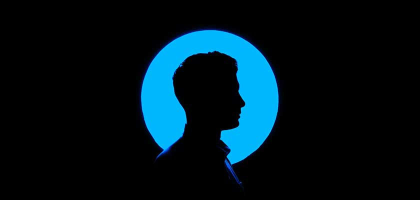 Silhouette of a person in profile against a bright blue circle on a black background, creating a mysterious and dramatic mood.