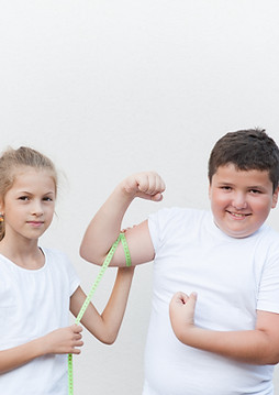 Dünnes-Mädchen-und-dicker-Junge-messen-ihre-Oberarme-es-ist-ein-lustiger-Wettkampf-die-beiden-Kinder-lächeln-und-strahlen-positive-Energie-Kraft-Zuversicht-und-Optimismus-aus-denn-Dicksein-und-Dünnsein-hat-keine-Auswirkung-auf-ihre-Lebensfreude-sie-sehen-selbstbewusst-aus-und-akzeptieren-ihren-Körper-und-spüren-ihre-Kraft.