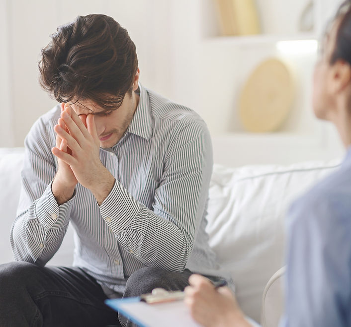 Ein-gestresster-Mann-sitzt-auf-einer-Couch-in-einer-psychotherapeutischen-Sitzung-er-schweigt-und-ist-in-sich-gekehrt-reflektiert-seine-Vergangenheit-bearbeitet-Kindheitserlebnisse-bewältigt-sein-Trauma-bekommt-neue-Perspektiven-zur-Lösung-seiner-Probleme-denkt-über-Beziehung-nach-kann-über-Schuld-vorwürfe-und-Selbstzweifel-nachdenken-die-Psychotherapeutin-hört-aufmerksam-zu-schenkt-dem-Klienten-Empathie-Respekt-und-Geduld-und-findet-wertschätzende-Worte-für-seine-mentale-Unterstützung-und-gibt-emotionalen-Halt.