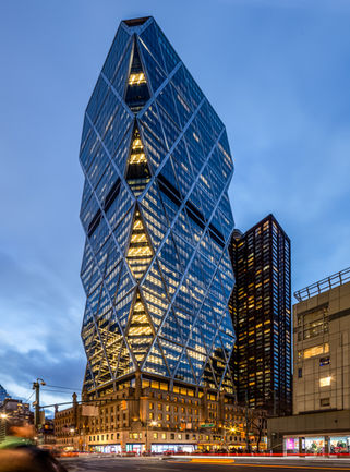 <img src=”illuminated-iconic-Hearst Tower-New York City .jpg” alt=”Exterior of Hearst Tower illuminated at night with light trails />