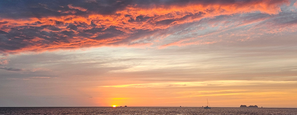 Orange sunset turns amber and purple in the sky with fading light glinting on the ocean beneath